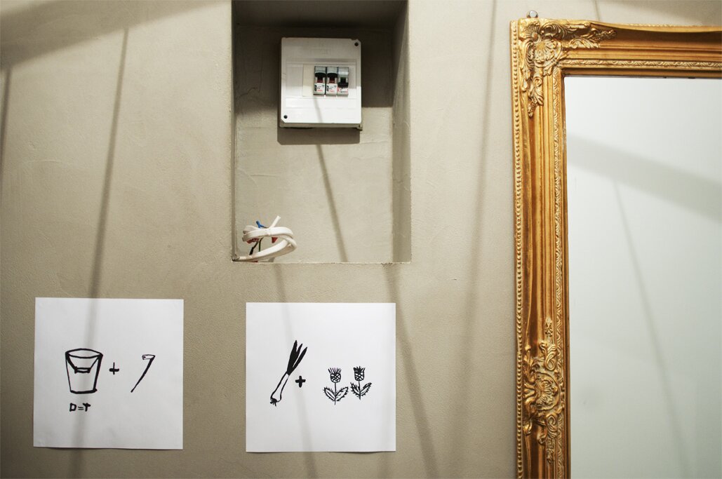 A photography of 2 rebus illustrations hanging on the wall, next to the mirror in a golden frame.