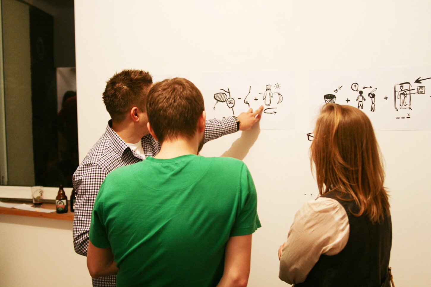 A photography of 3 people looking at a rebus illustration hanging on the wall.